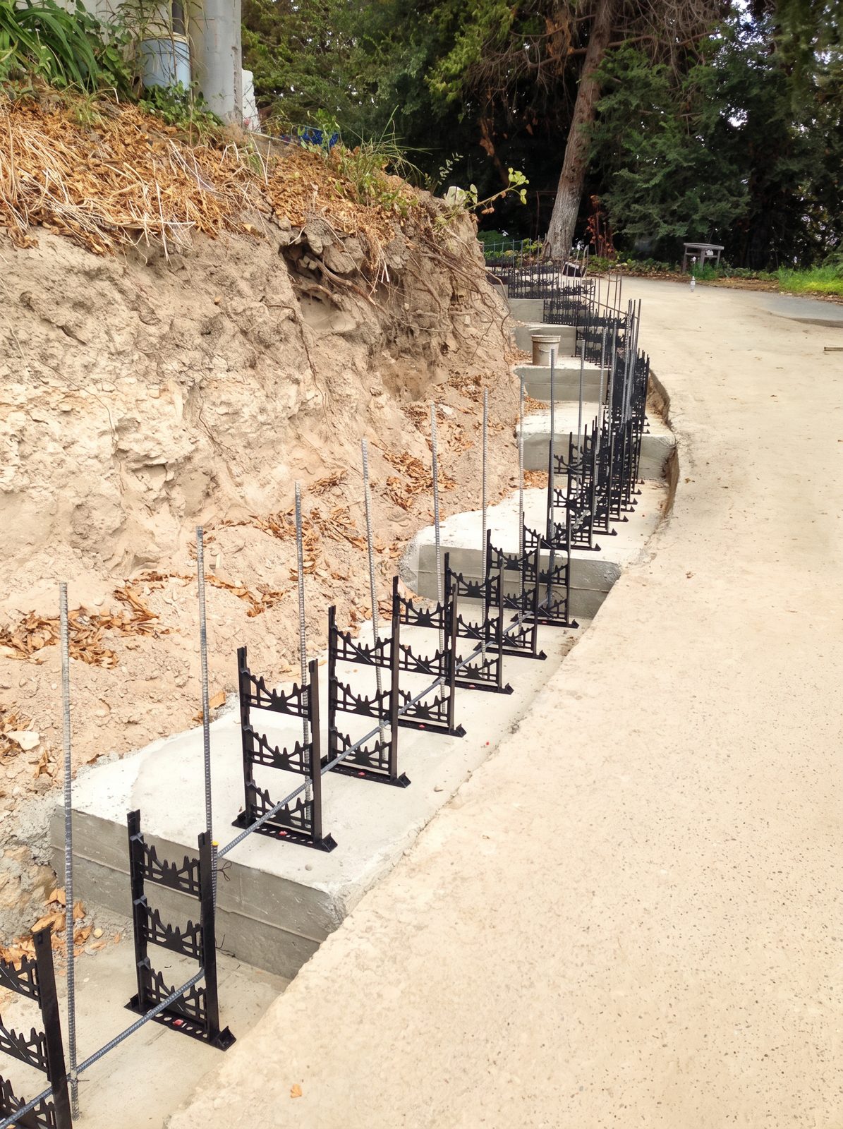 Stepped concrete footings with vertical rebar and wall form ties along a hillside