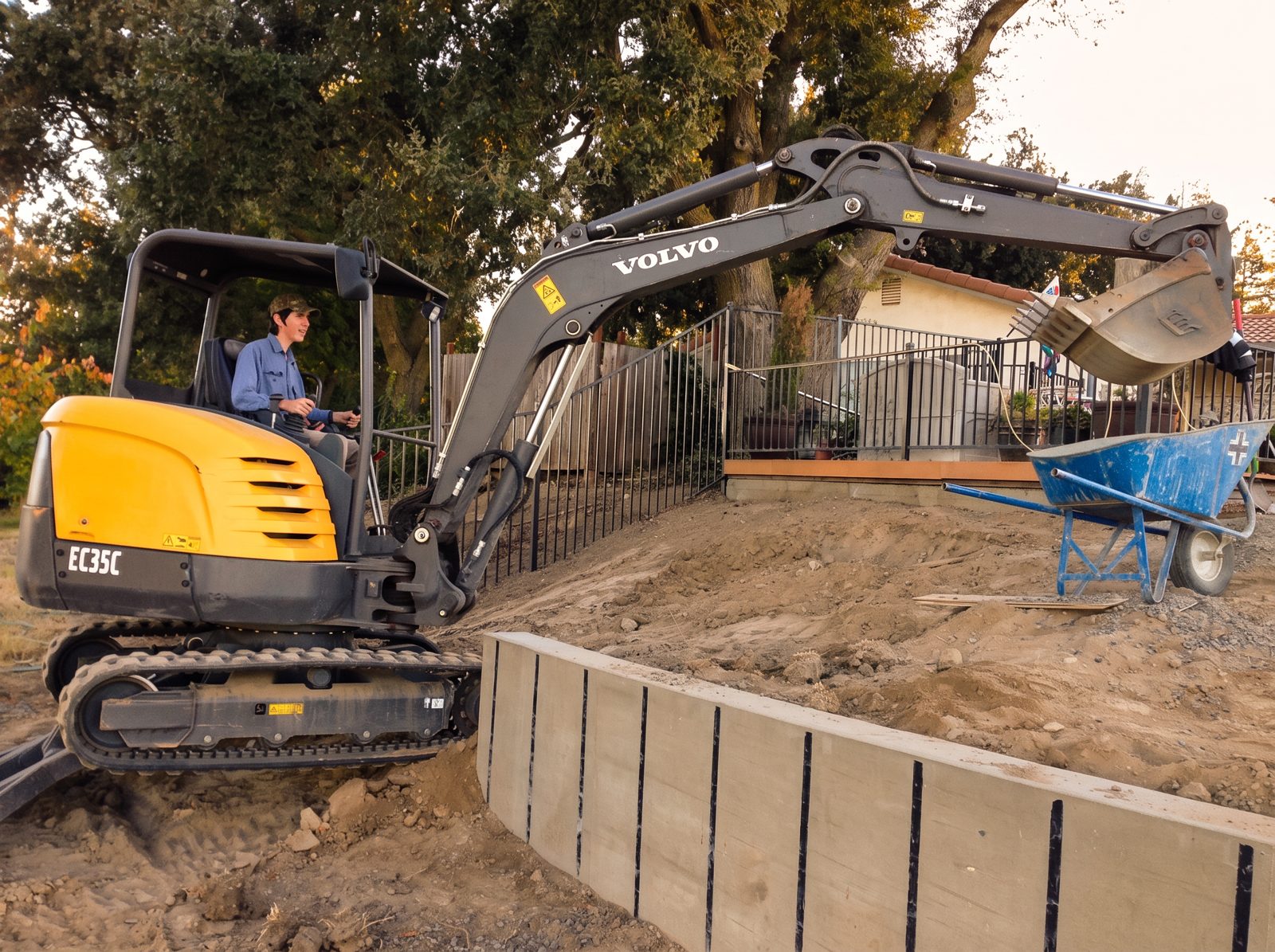 Ultimate Concrete crew member on a mini excavator beside a finished concrete retaining wall